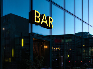 Bar sign and entrance at the business district at dusk, blue sky and buildings reflected on the glass facade