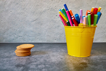 Yellow glass filled with colored pencils and cookies for children . Copy space and background