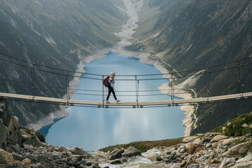 Girl traveler with a backpack in the mountains. A young girl stands on a suspension bridge on a background of mountains and glaciers. Travel and active life concept. Adventure trip to Europe.