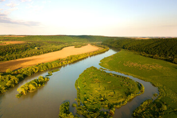 Aerial view of bright river flowing through green meadows in spring.