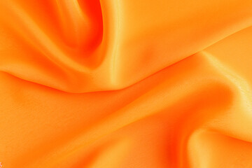 Satin silk fabric orange color for the background. Crumpled wavy silk. Texture of satin fabric