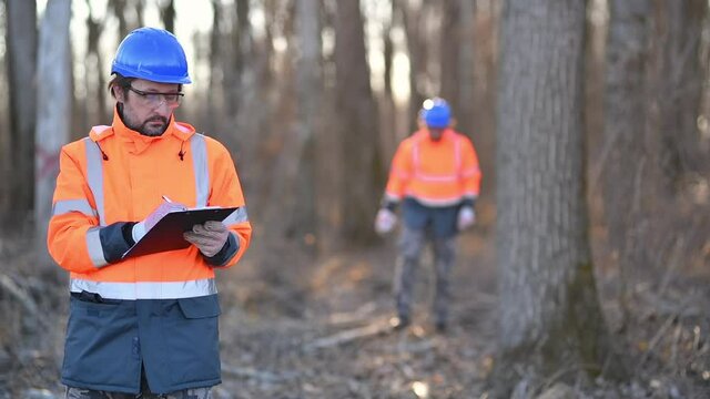 Forestry technician writing notes on clipboard notepad paper in forest