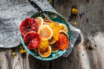 Ceramic bowl with mini pancakes, blood orange slices, orange jam and honey on old wooden table.