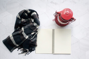 Top view of the a black scarf, candle and a notebook on the table, on the tray. Marble background.