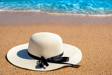 Fototapeta na wymiar White woman straw hat laying on tropical sand beach with blue vibrant ocean water in background on sunny summer day. Vacations and destination travel concept.