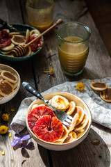 Ceramic bowl with mini pancakes, blood orange slices and honey on old wooden table.