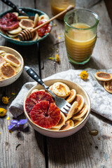 Ceramic bowl with mini pancakes, blood orange slices and honey on old wooden table.