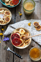 Ceramic bowl with mini pancakes, blood orange slices and honey on old wooden table.