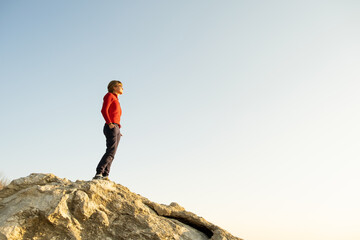 Obraz premium Young woman hiker standing alone on big stone in morning mountains. Female tourist on high rock in wild nature. Tourism, traveling and healthy lifestyle concept.