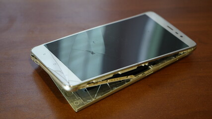 Swollen smartphone battery. Damaged smartphone with a faulty battery. Damaged phone on a wooden background.