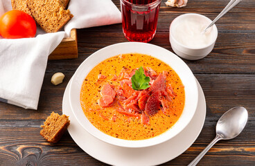 soup , traditional red borscht with sour cream and parsley in a white plate, spoon, bread, tomatoes on a brown wooden background,