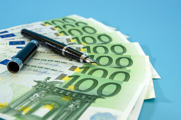 black pen and 100 euro banknotes. Blue background. Business concept.