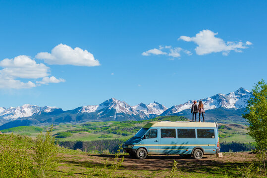 couple standing on top of a camper van in front of mountain range