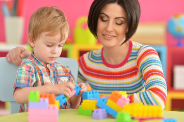 Young mother and cute little son playing with colorful plastic blocks