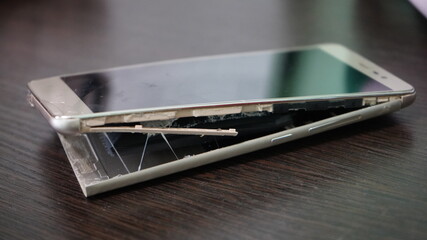 Swollen smartphone battery. Damaged smartphone with a faulty battery. Damaged phone on a wooden background.