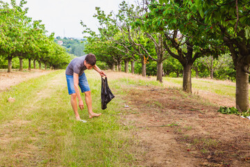 A man collects trash in the garden. People leave a lot of trash