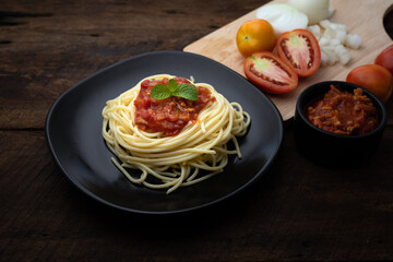 Italian pasta spaghetti with tomato sauce and herbs on a black plate a plate on dark woonen background with copy space for your text