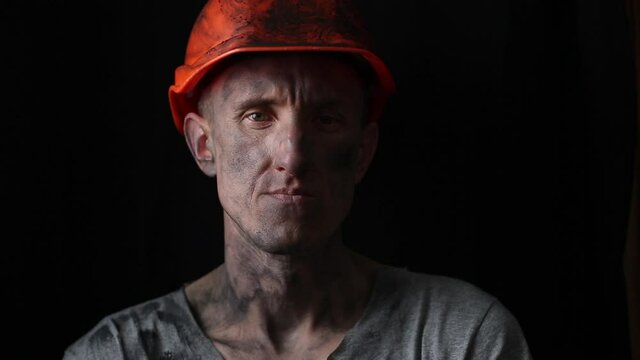 The face of a male miner in a helmet on a black background. Portrait of a tired mining worker.