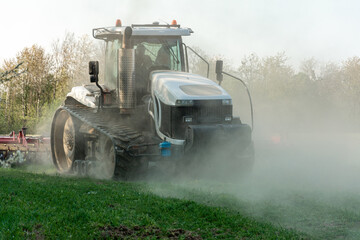 Fototapeta premium In the spring, a farmer pulls harrows with a modern tractor and sows a field with beets. Sowing campaign on agricultural land during tillage.