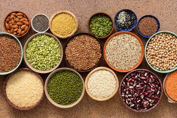 Assorted of a varied of legumes, beans, grains and seeds in bowls on a brown stone background. Top view, flat lay