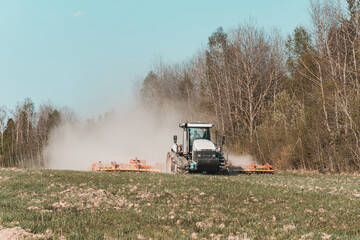 Fototapeta premium In the spring, a farmer pulls harrows with a modern tractor and sows a field with beets. Sowing campaign on agricultural land during tillage.