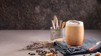 Latte or cappuccino with milk foam and lavender in a glass with coffee beans. Dark background - obrazy, fototapety, plakaty