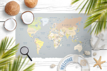 World map on a white wooden table surrounded with coconut, palm leaves, shells, starfish, lifebelt, anchor, magnifier. Concept of travel and finding tropical destinations
