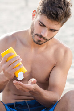 young man applying suncream on the beach