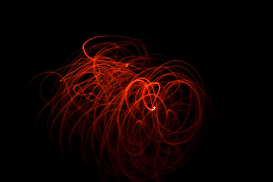 Abstract fine art design produced by long exposure shot of glowing ember of incense stick and red LED neon light on black background at night. Soft focus due to long exposure.