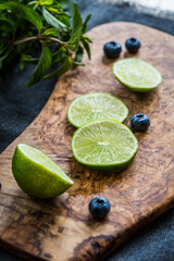 Sliced key lime and few blueberries on wooden board on  dark background.