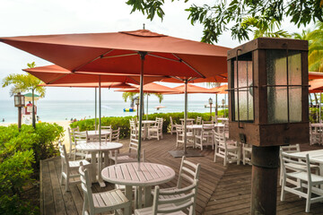 Montego Bay, Jamaica. Restaurant terrace on the beach with large orange patio umbrellas and empty tables and chairs. Ocean in background.