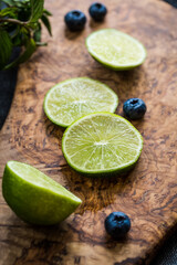 Sliced key lime and few blueberries on wooden board on  dark background.