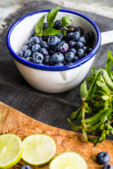 White ladle with fresh juicy blueberries and bunch of mint on black fabric.