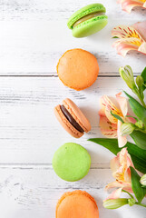 French cookies top view, few beige, yellow and green French macaroons and yellow Alstroemeria flowers on a white wooden background