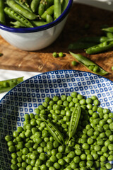 Fresh green pea in blue and white plate and pea pods in white metal ladle on wooden board  on white background.