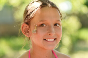 
Portrait of a beautiful girl with a snail. A snail on the face of a child. A young girl is playing with a snail. Summer walks in the park.