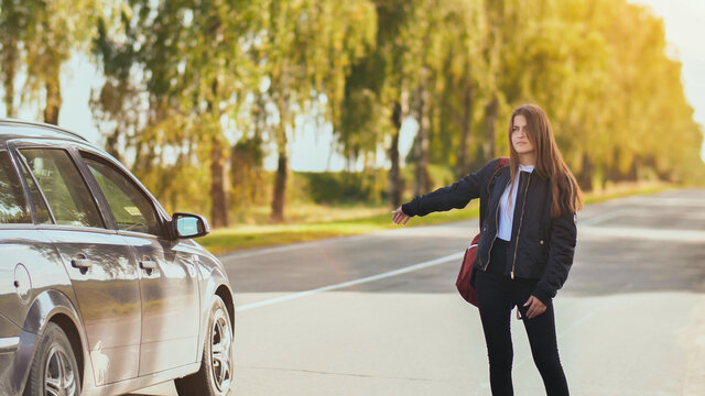 A young girl stands on the road and tries to stop any car.