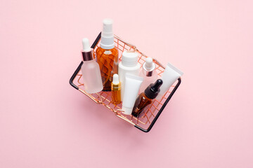 Shopping basket full of cosmetic bottles and packaging on pink background, view from above....