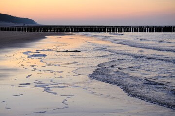 Beautiful sunset colors on the beach of sea and amazing reflection in water. Silhouette of breakwater on horizon.