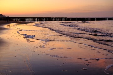 Beautiful sunset colors on the beach of sea and amazing reflection in water. Silhouette of breakwater on horizon.