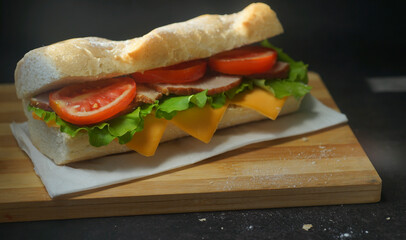 An appetizing sandwich with ham, cheese, tomatoes and lettuce lies on a board with egg and lemon  on black background