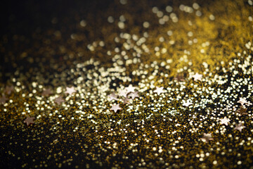 Beautiful Christmas light background. Abstract glitter bokeh and scattered sparkles in gold color, on black