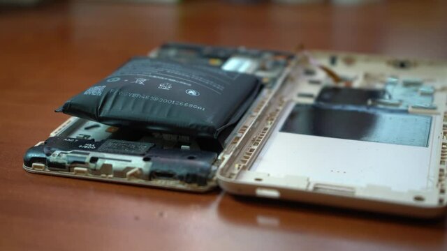 Swollen smartphone battery. Damaged smartphone with a faulty battery. Damaged phone on a wooden background.