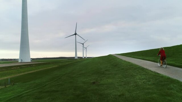 WS POV TS Girl (10-11) cycling on dyke between wind turbines / Urk, Flevoland, Netherlands