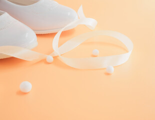 Pair of white baby lacquered girls shoes with beige ribbon and white balls at peach background with place for text