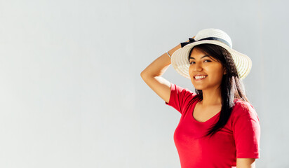Naklejka premium Brunette Latin woman in profile holding a hat with one hand on her head and smiling