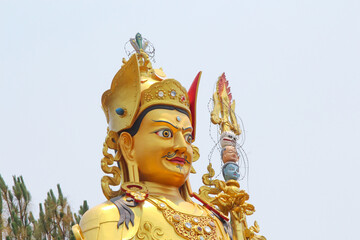 Head of large gold colored Guru Rinpoche (also known as Padmasambhava) statue in sunny day in...