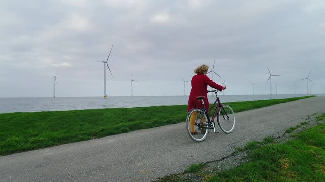 WS POV Girl (10-11) walking with bicycle on dyke next to wind turbines / Urk, Flevoland, Netherlands