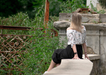 The blond-haired girl sits on a stone railing and looks back.