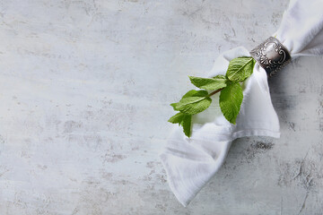A white cotton napkin is connected by an antique metal ring. Decorative items on a light textured...